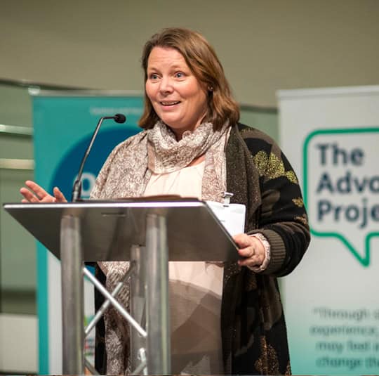 Joanna Scanlan gives a speech in front of an Advocacy Project banner