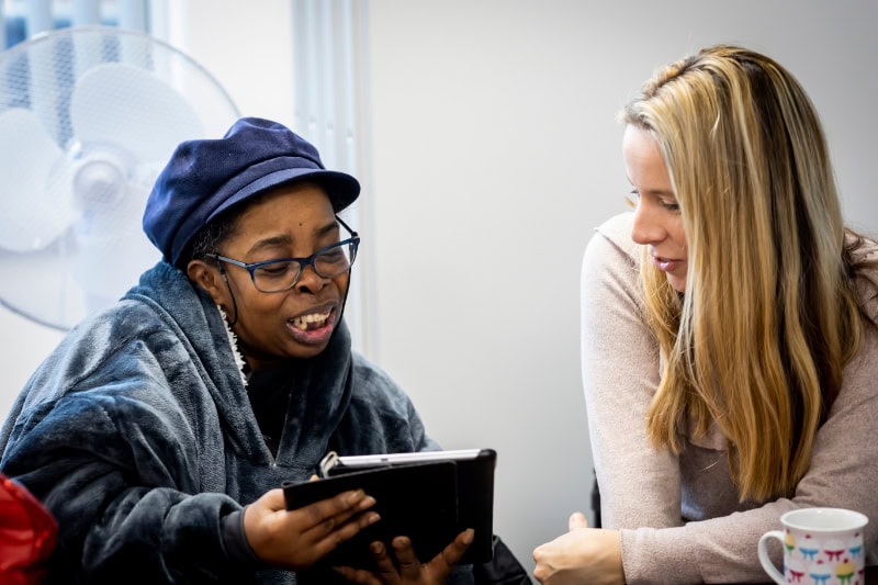 Two women talking, one holding a tablet.