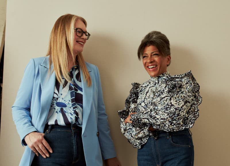 Two women standing against a wall and smiling