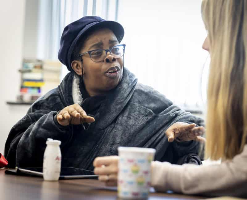 A woman at a table talks animatedly to another woman seen from behind